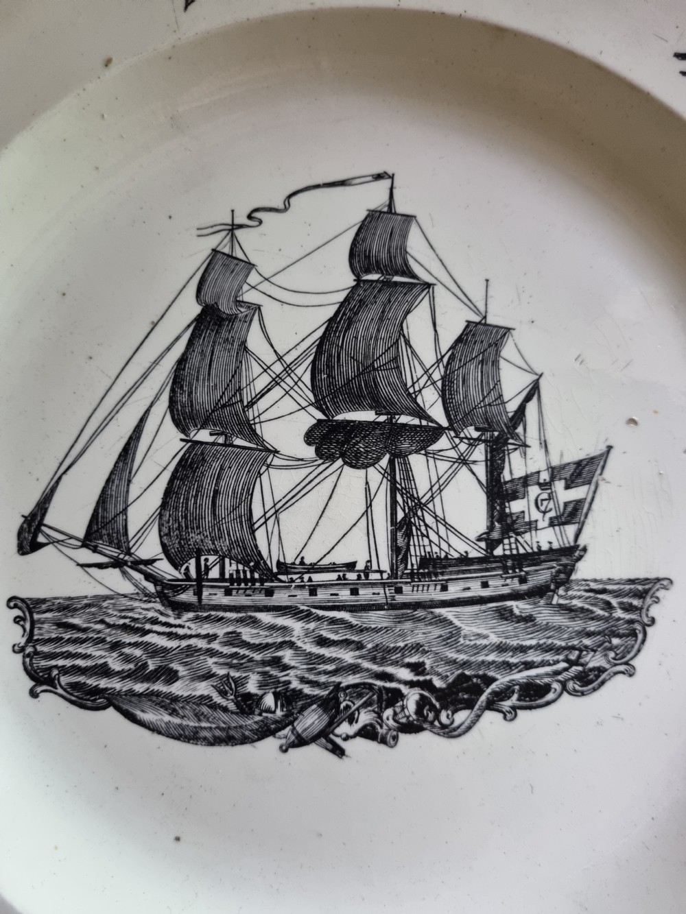 A late eighteenth or early nineteenth-century scalloped creamware plate featuring a central black transfer-printed sailing ship surrounded by floral border sprays. View II