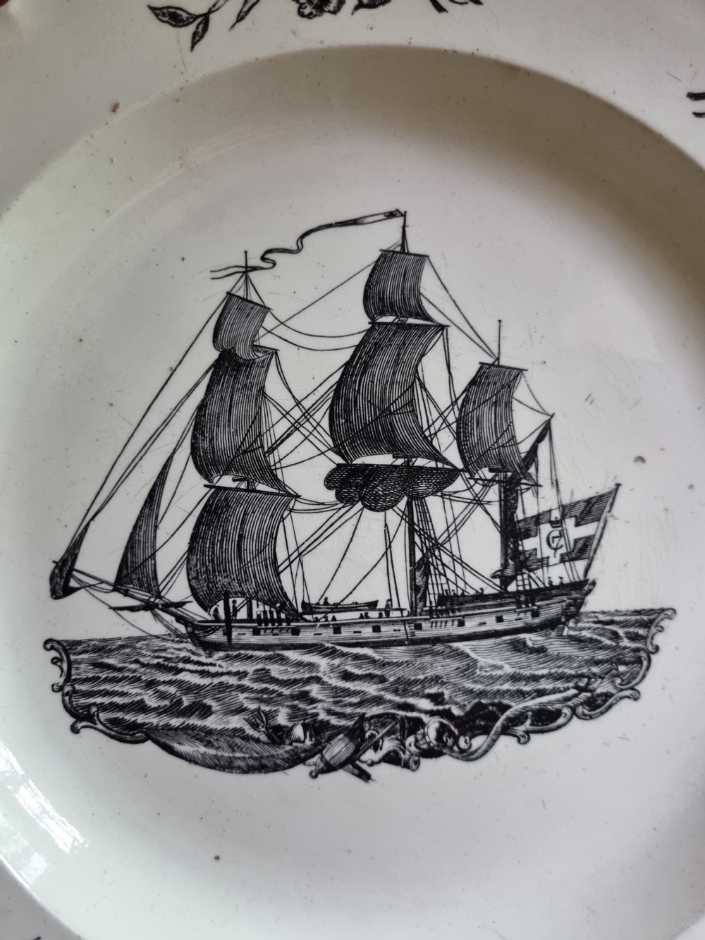 A late eighteenth or early nineteenth-century scalloped creamware plate featuring a central black transfer-printed sailing ship surrounded by floral border sprays. View VII