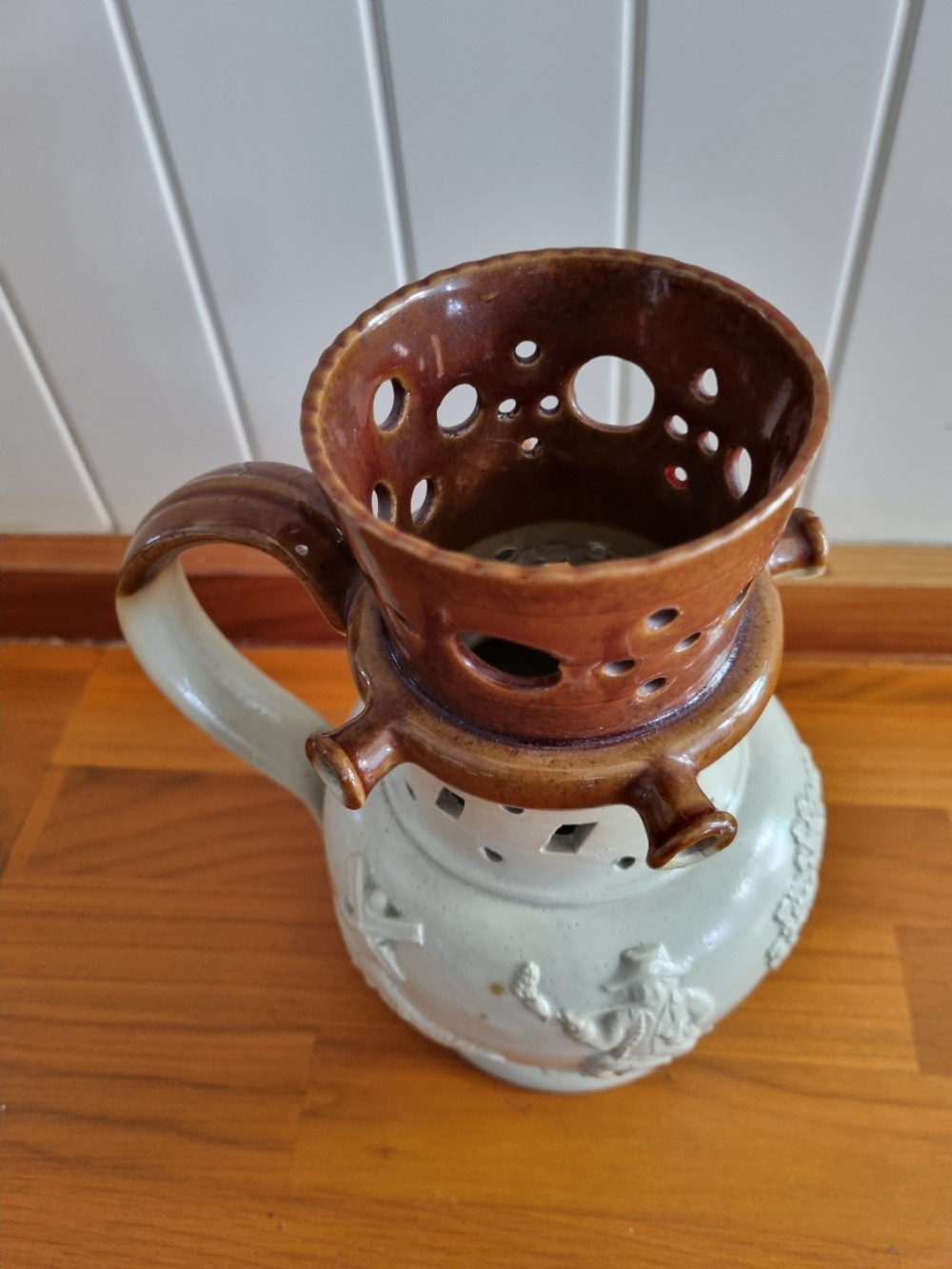 A 19th-century salt-glazed stoneware puzzle jug featuring a brown pierced upper neck, a cream body with a windmill relief decoration, and a hollow loop handle. View V