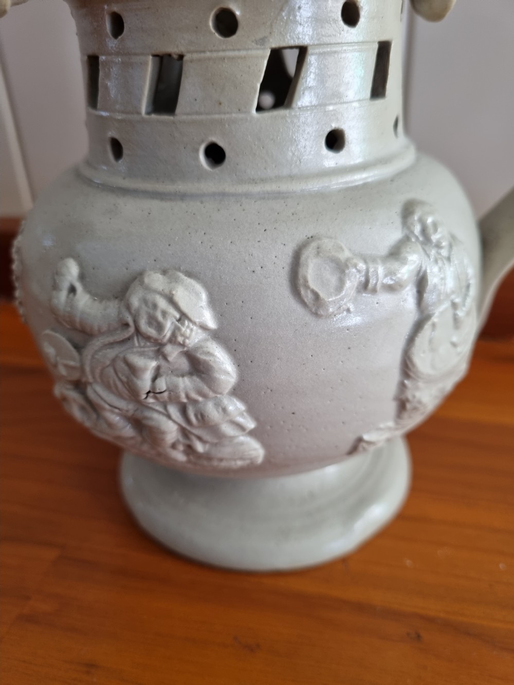 A 19th-century salt-glazed stoneware puzzle jug featuring a brown pierced upper neck, a cream body with a windmill relief decoration, and a hollow loop handle. View VI