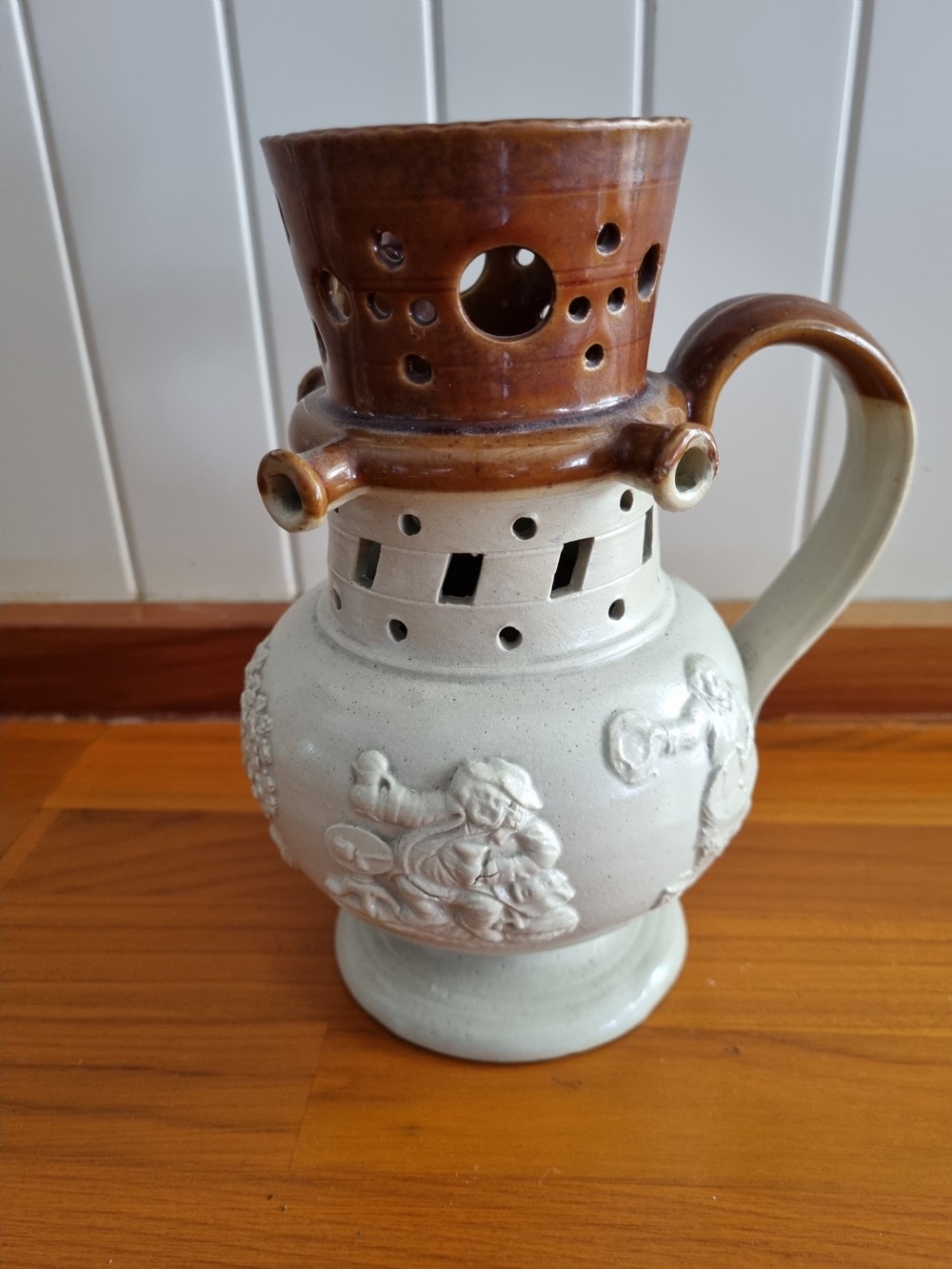 A 19th-century salt-glazed stoneware puzzle jug featuring a brown pierced upper neck, a cream body with a windmill relief decoration, and a hollow loop handle. View VIII