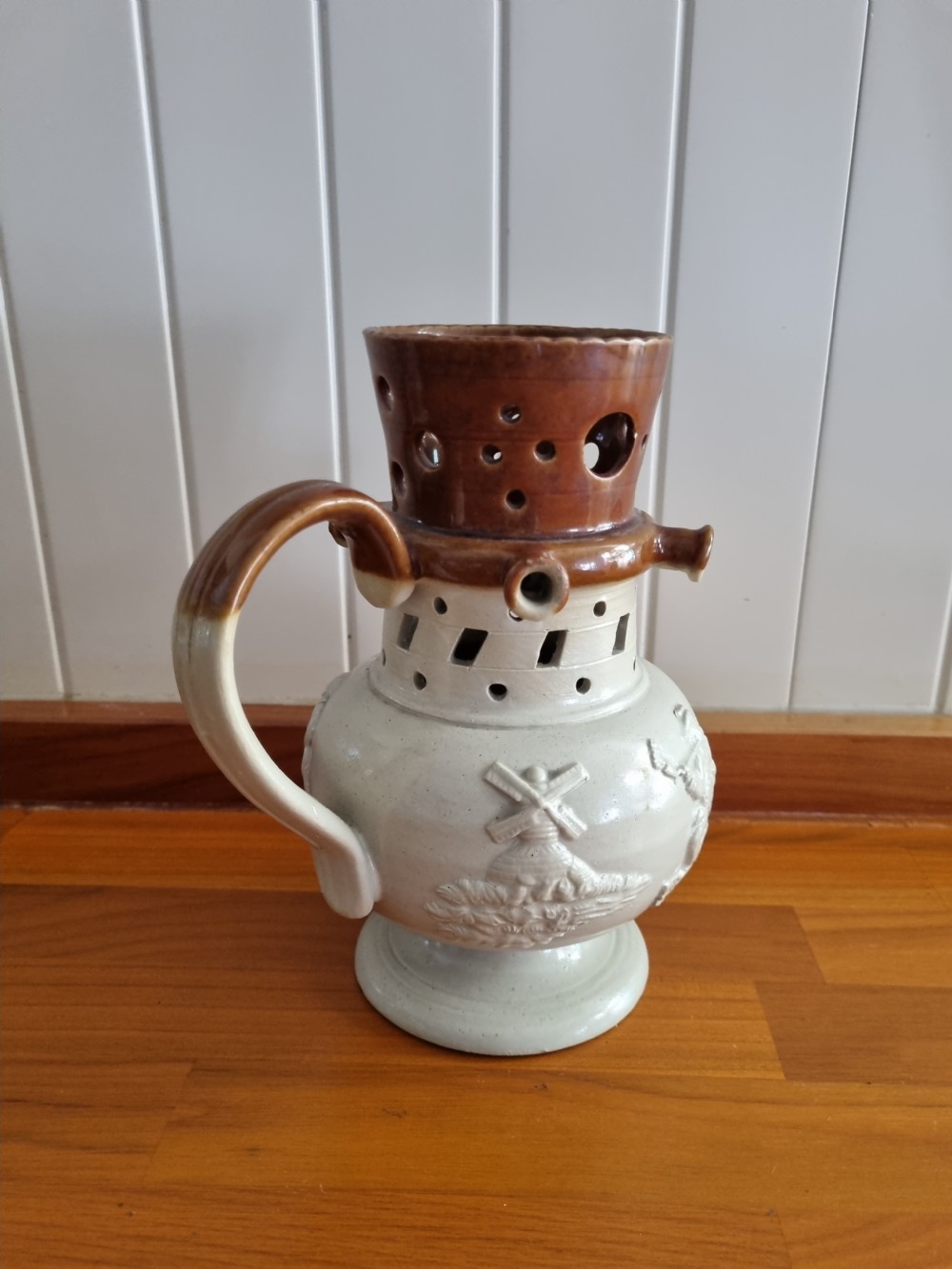 A 19th-century salt-glazed stoneware puzzle jug featuring a brown pierced upper neck, a cream body with a windmill relief decoration, and a hollow loop handle. View IX