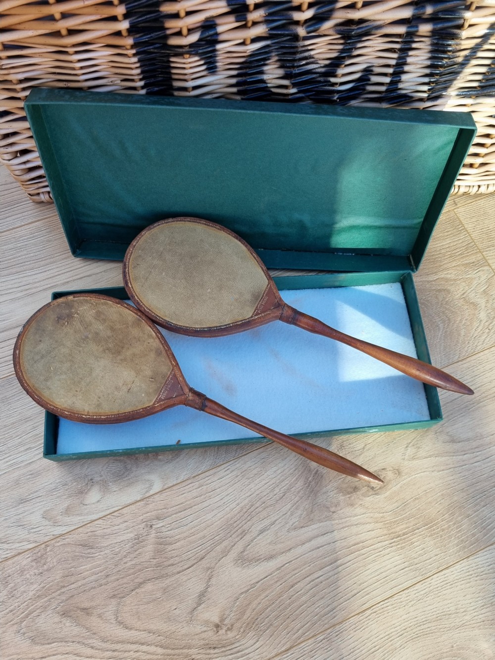 Pair of antique vellum ping pong bats with turned wooden handles displayed inside an open dark green box. View V