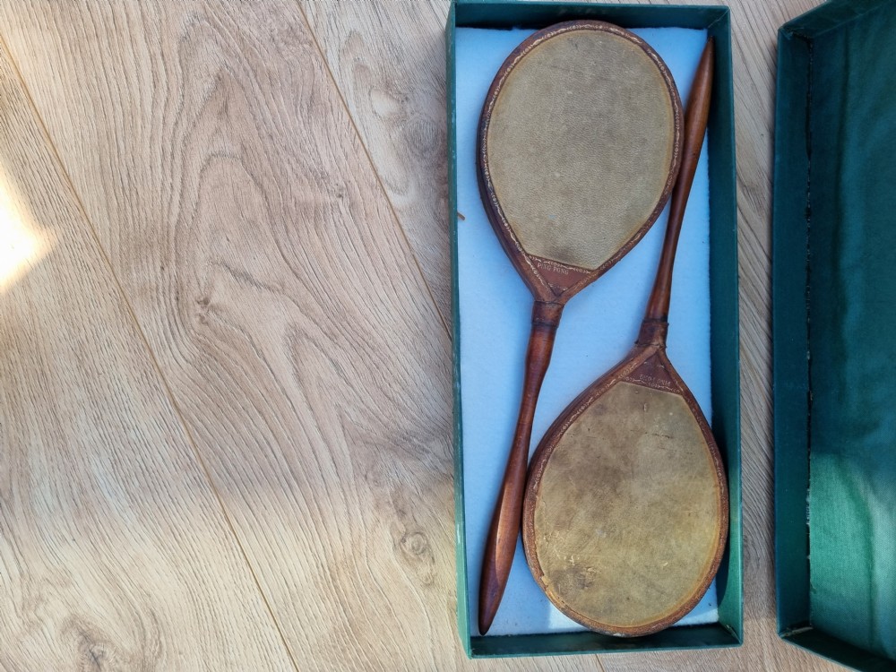 Pair of antique vellum ping pong bats with turned wooden handles displayed inside an open dark green box. View VI