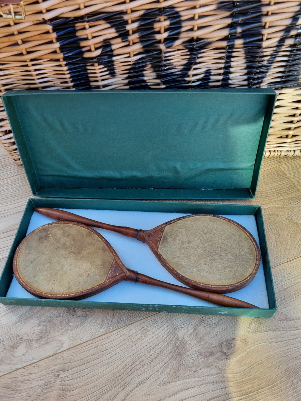 Pair of antique vellum ping pong bats with turned wooden handles displayed inside an open dark green box. View VII