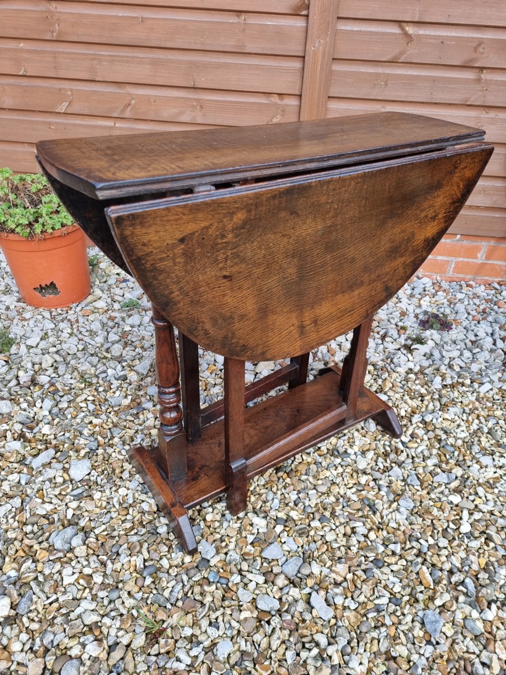 An eighteenth-century dark oak gateleg table featuring drop-down oval leaves, turned column supports, and a flat sleigh base. View II