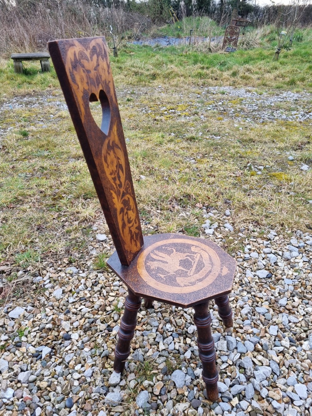 A 19th-century Welsh folk art spinning chair with a tall back featuring a heart cut-out, floral pyrography, a hexagonal seat with a carved dragon motif, and four turned legs. View IV