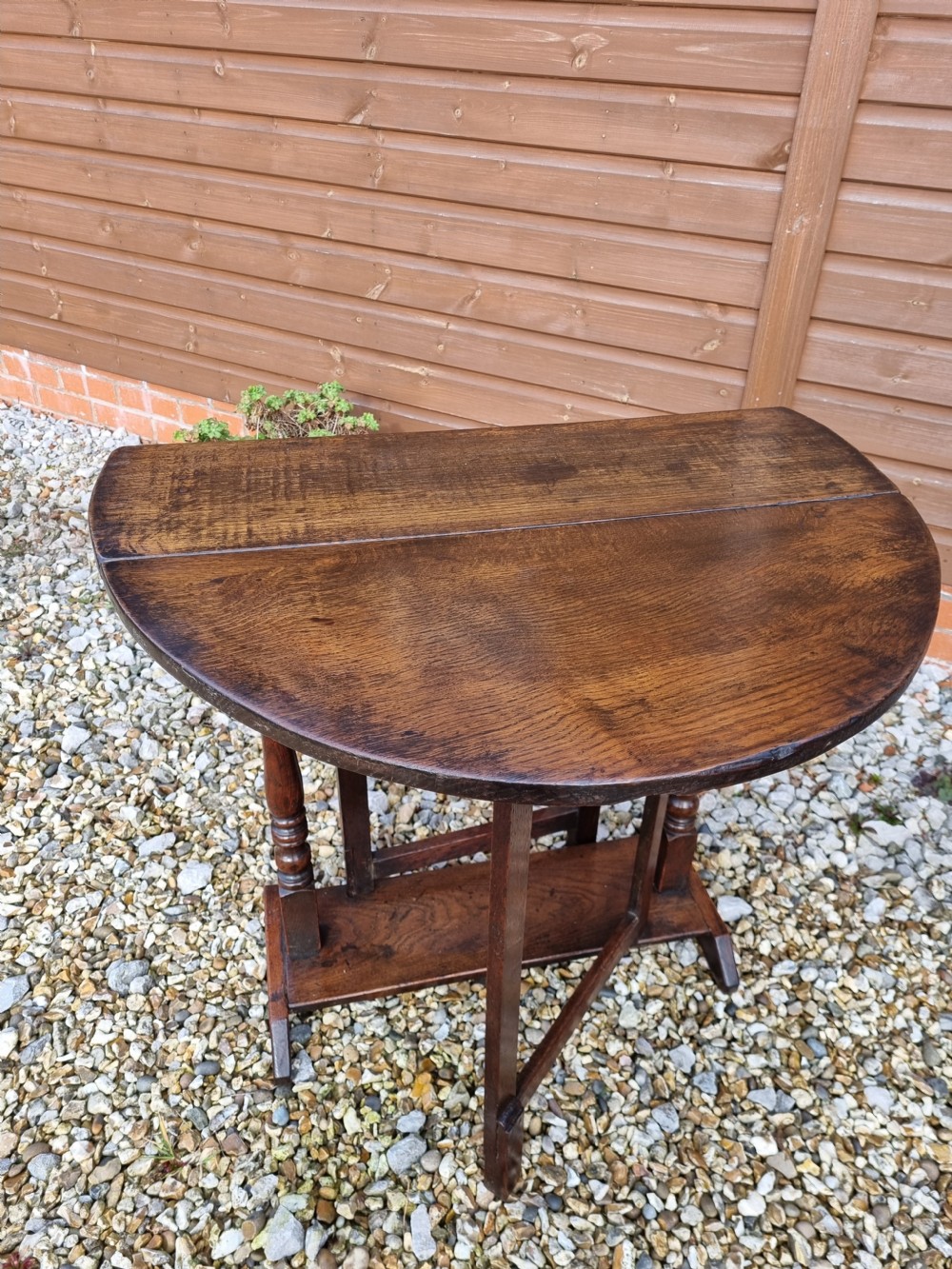 An eighteenth-century dark oak gateleg table featuring drop-down oval leaves, turned column supports, and a flat sleigh base. View X