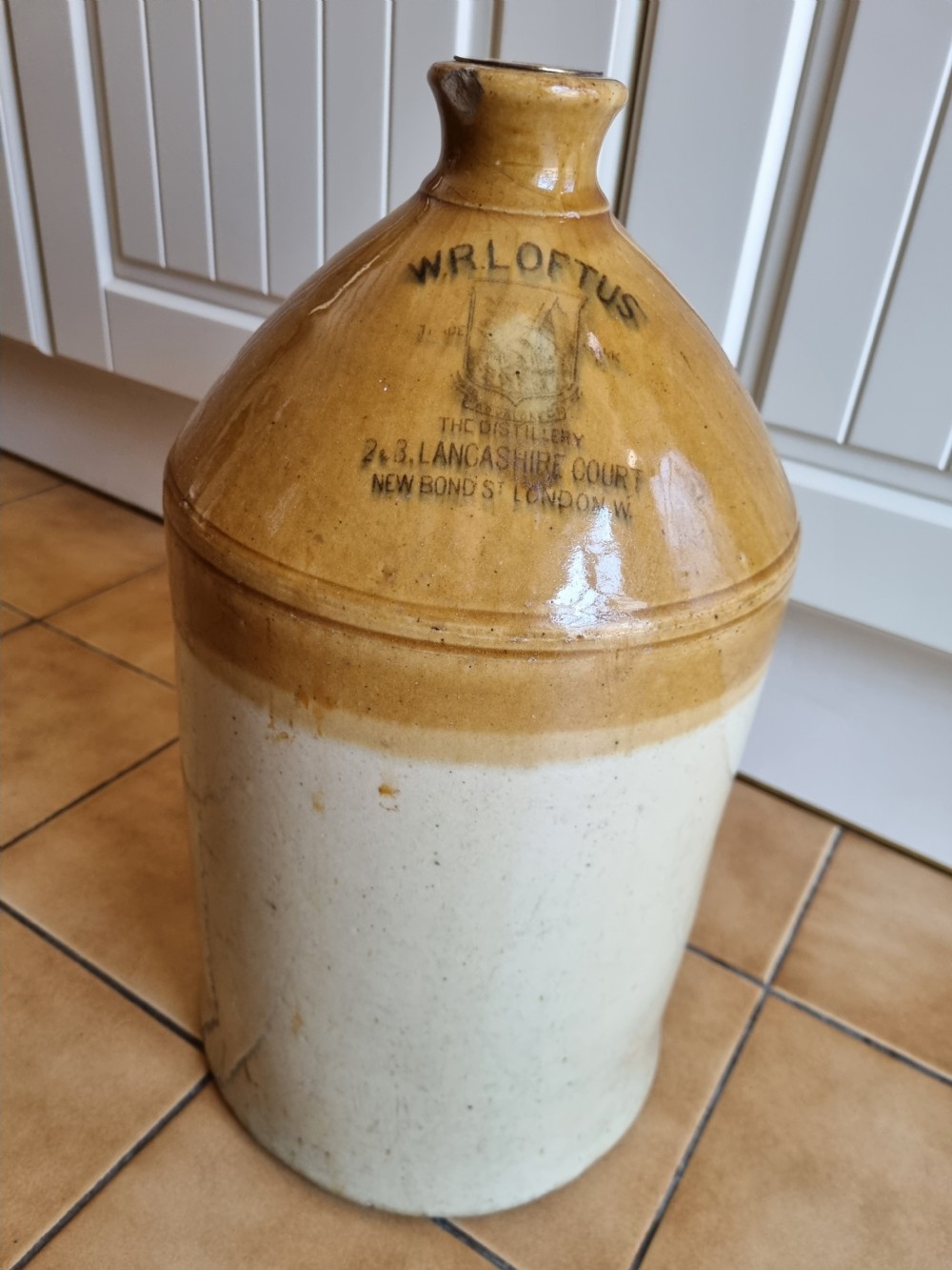 A nineteenth-century two-tone stoneware spirit jug featuring a brown glazed upper section with stamped text reading W.R. Loftus London above an off-white lower section.