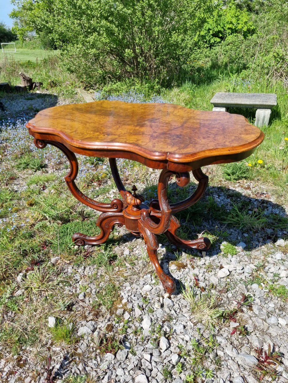 An antique Victorian burr walnut centre table with a scalloped serpentine top, wood inlay detail, and a carved four-legged base. View III