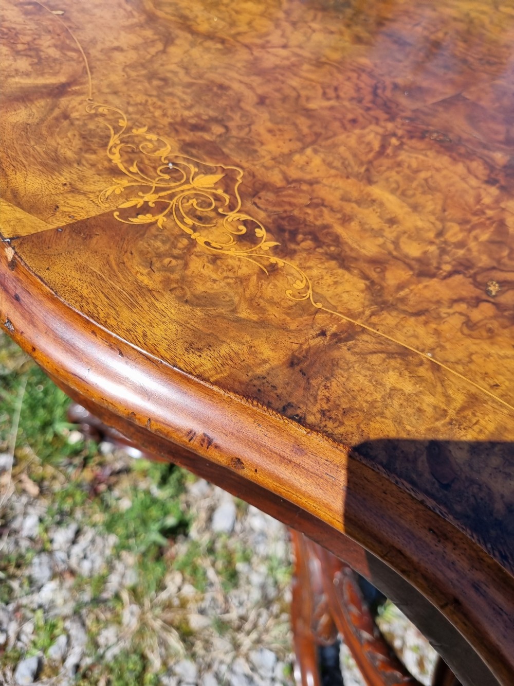 An antique Victorian burr walnut centre table with a scalloped serpentine top, wood inlay detail, and a carved four-legged base. View V