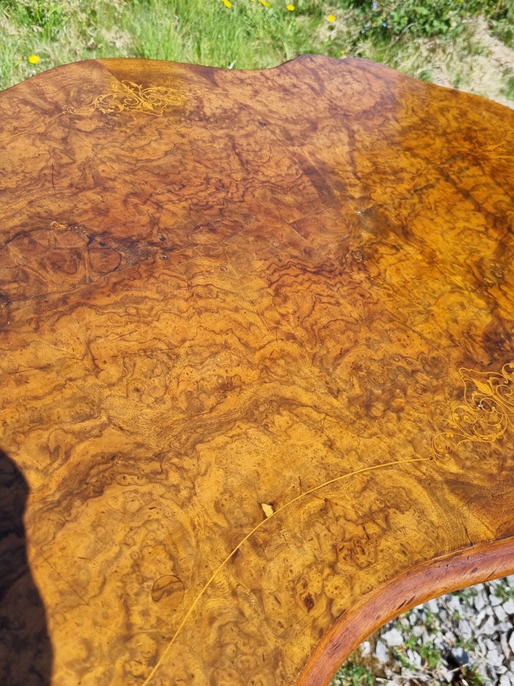 An antique Victorian burr walnut centre table with a scalloped serpentine top, wood inlay detail, and a carved four-legged base. View VI