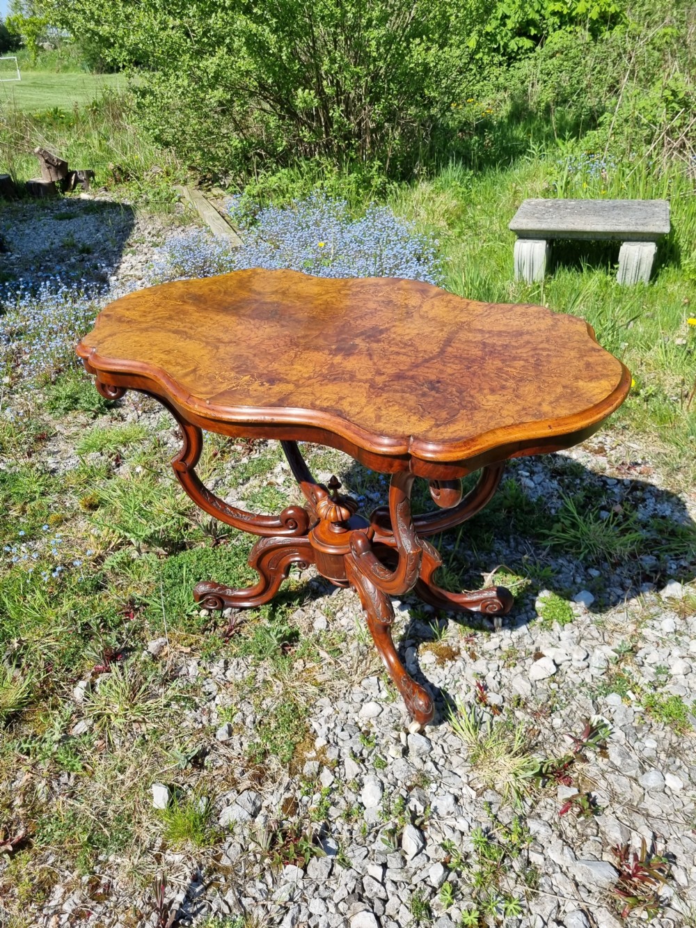An antique Victorian burr walnut centre table with a scalloped serpentine top, wood inlay detail, and a carved four-legged base. View VII
