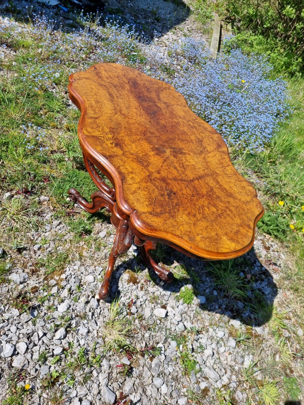 An antique Victorian burr walnut centre table with a scalloped serpentine top, wood inlay detail, and a carved four-legged base. View IX