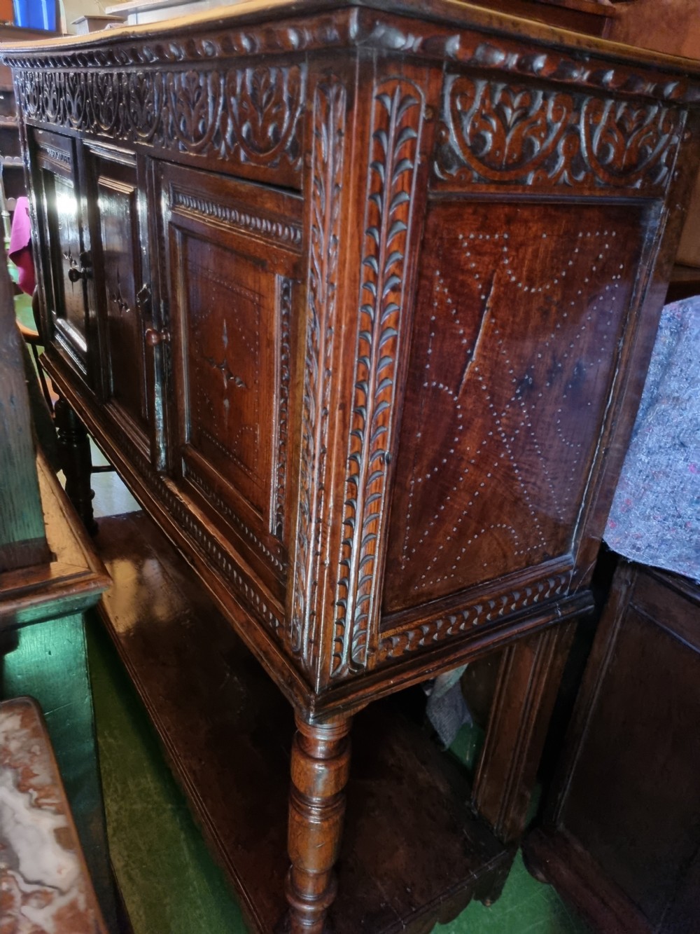 A 17th-century dark oak Lancashire buffet cupboard featuring three carved star-motif panel doors above turned support columns and a lower pot board shelf. View IX