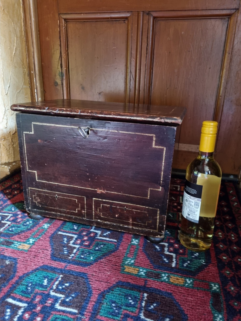 A 19th-century small dark painted Welsh coffer featuring geometric line-painted panel details, a hinged lid, and a key inserted into the front keyhole. View II