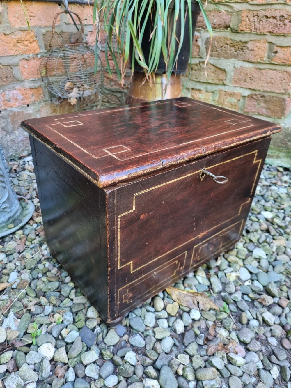 A 19th-century small dark painted Welsh coffer featuring geometric line-painted panel details, a hinged lid, and a key inserted into the front keyhole. View V
