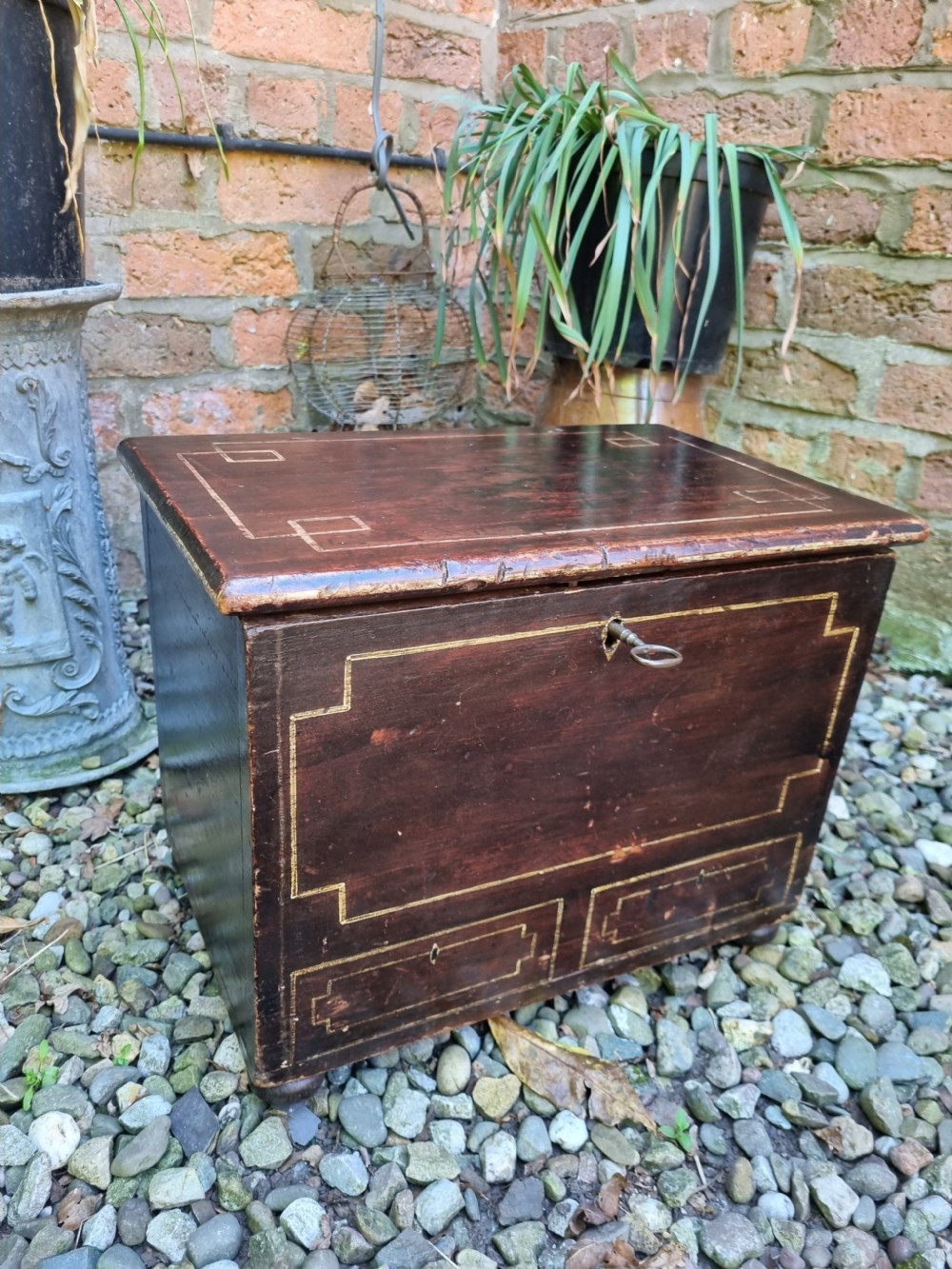 A 19th-century small dark painted Welsh coffer featuring geometric line-painted panel details, a hinged lid, and a key inserted into the front keyhole. View VII