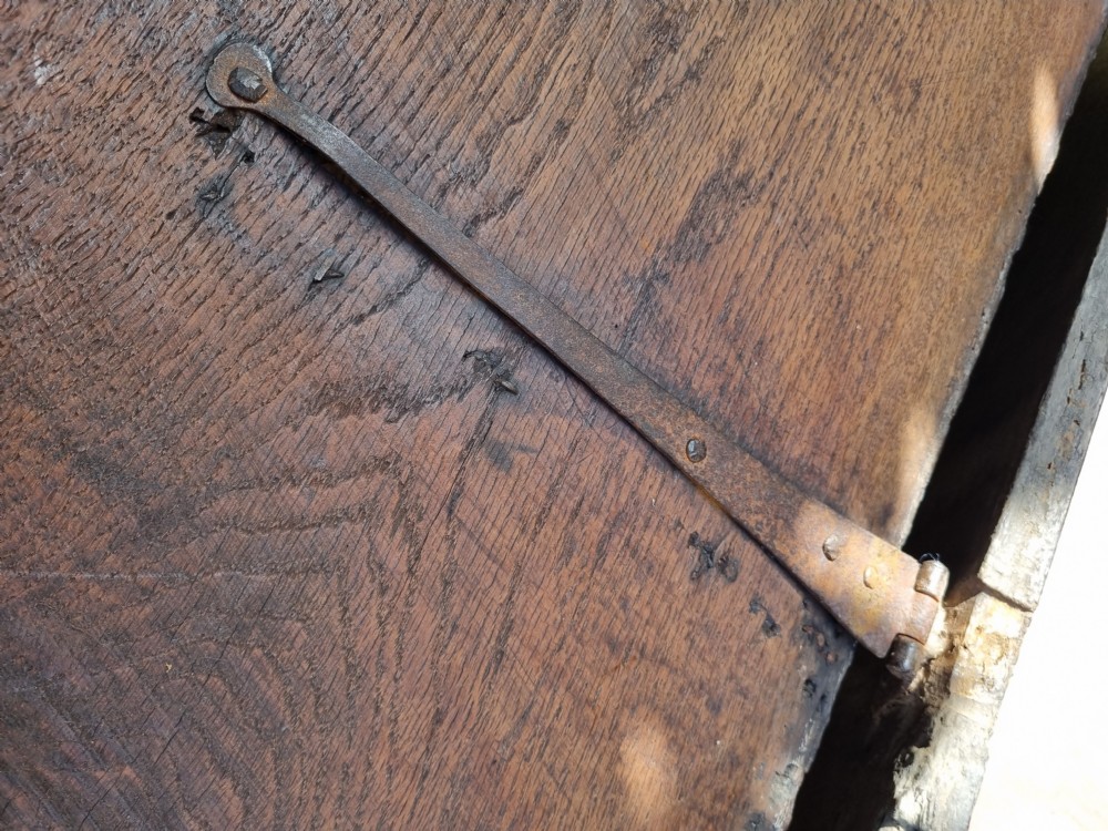 A late 17th-century dark oak coffer featuring a hinged lid, iron lockplate, and relief-carved front panel with foliate scroll motifs. View V