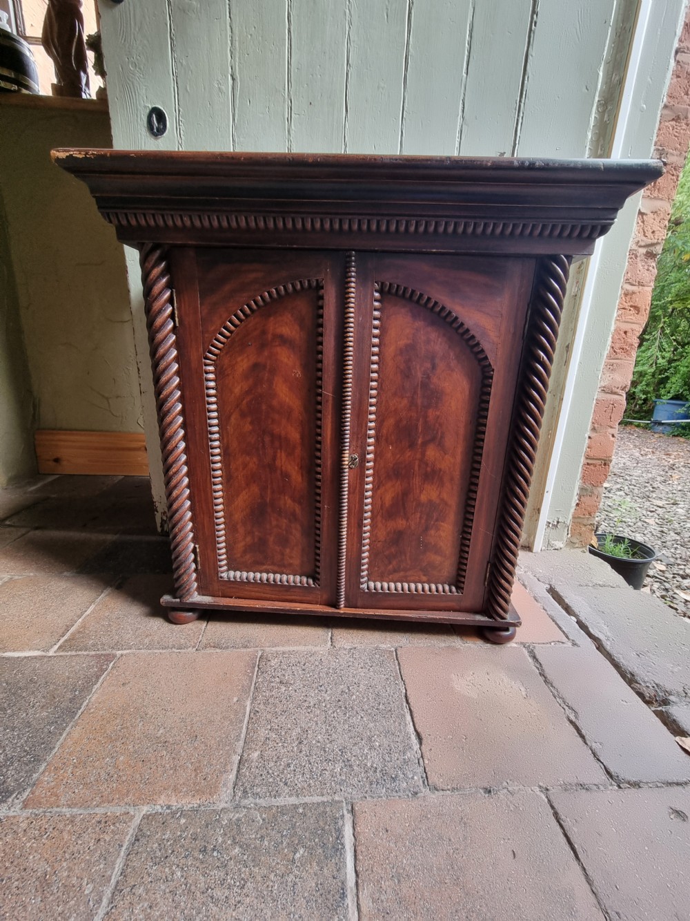 A 19th-century dark brown painted pine cupboard featuring double arched-panel doors, rope-twist corner columns, and beaded decorative trim. View VIII