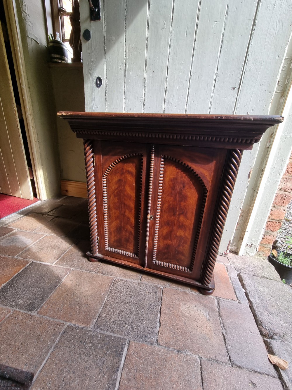 A 19th-century dark brown painted pine cupboard featuring double arched-panel doors, rope-twist corner columns, and beaded decorative trim. View VII