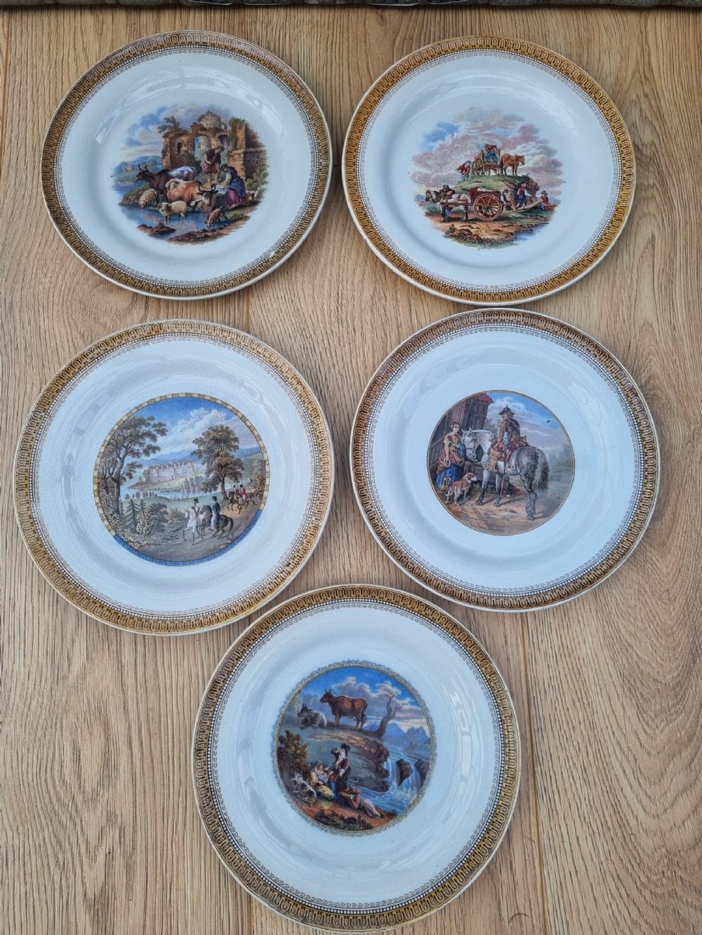 A set of five circular Victorian Prattware ceramic plates featuring polychrome transfer-printed pastoral landscape scenes with decorative gold geometric borders.