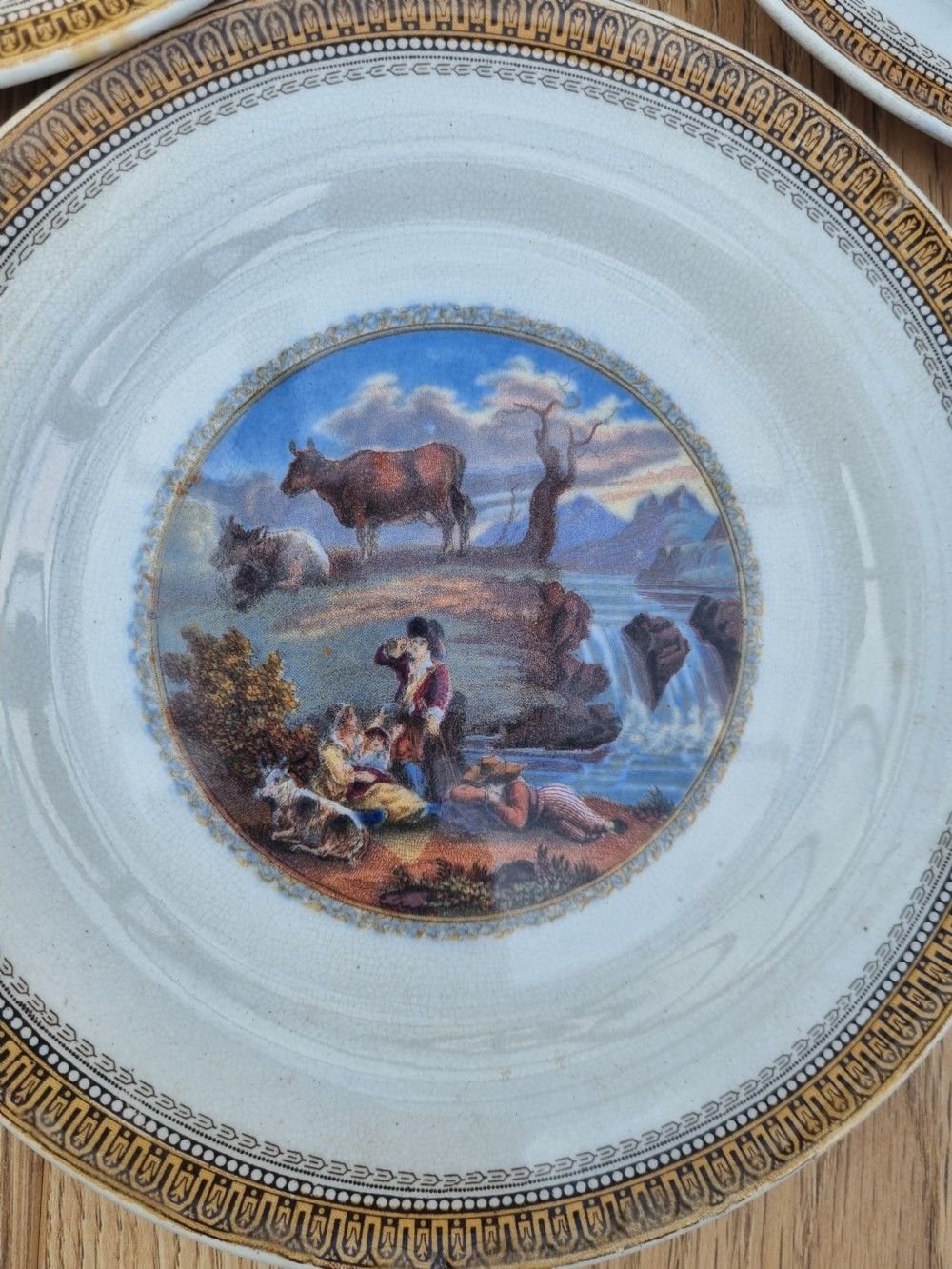 A set of five circular Victorian Prattware ceramic plates featuring polychrome transfer-printed pastoral landscape scenes with decorative gold geometric borders. View II