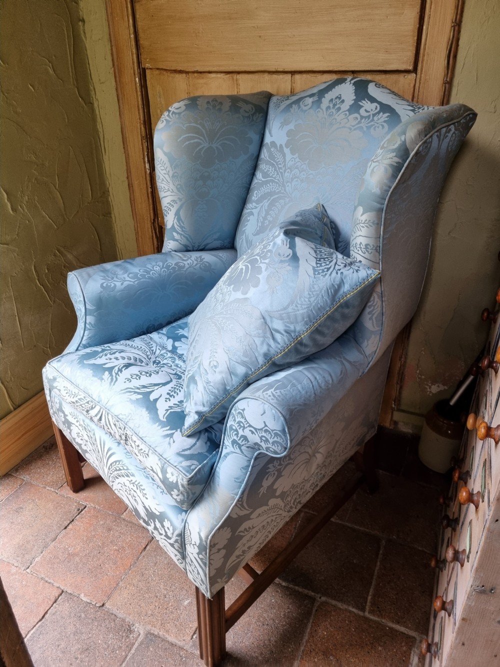 An antique high-backed wing armchair upholstered in ice blue patterned damask fabric with tapered square mahogany legs. View II
