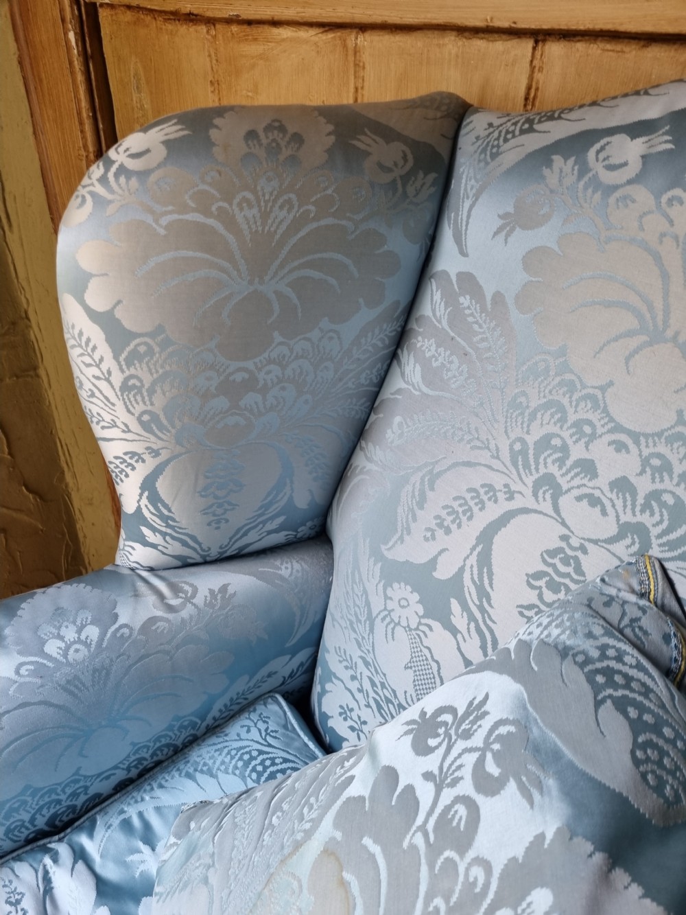 An antique high-backed wing armchair upholstered in ice blue patterned damask fabric with tapered square mahogany legs. View III