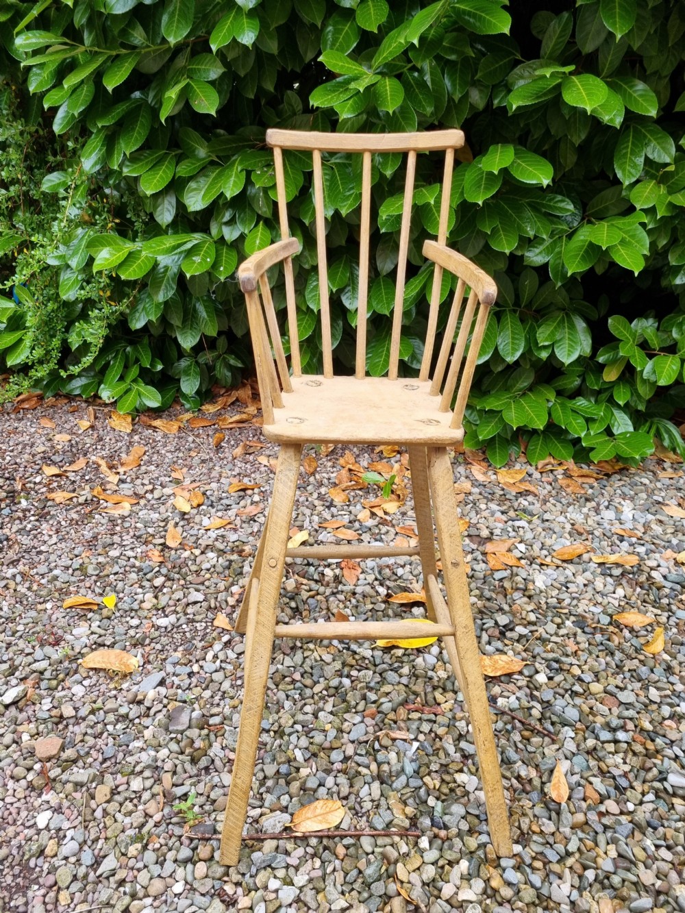 A 19th-century naive childs high chair made from natural ash and elm wood, featuring a spindle back, armrests, and splayed legs with stretchers. View III