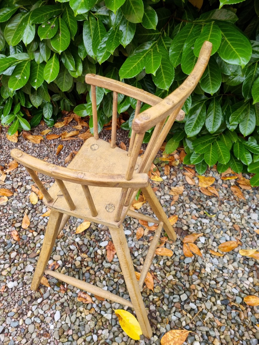 A 19th-century naive childs high chair made from natural ash and elm wood, featuring a spindle back, armrests, and splayed legs with stretchers. View V