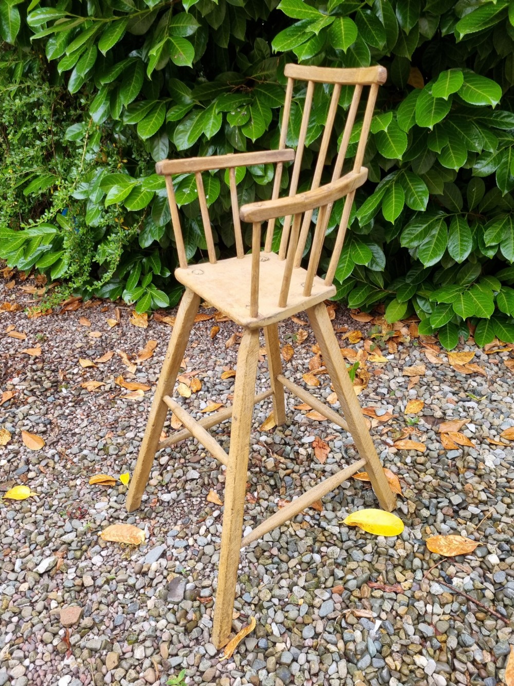 A 19th-century naive childs high chair made from natural ash and elm wood, featuring a spindle back, armrests, and splayed legs with stretchers. View VI