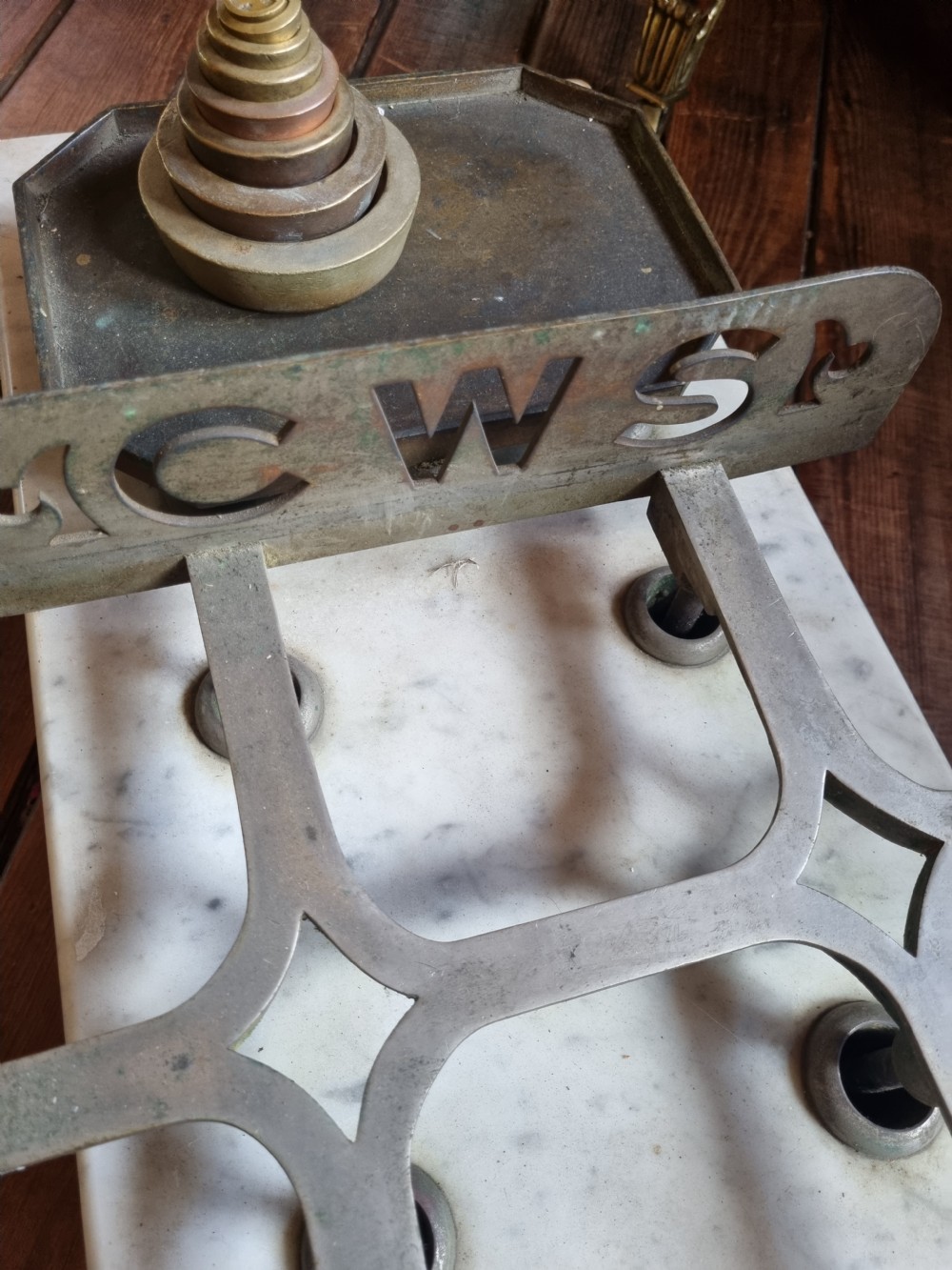 A Victorian grocer balance scale featuring a wooden base with gilded Equity lettering, a white marble slab surface, cast metal framework marked CWS, and nested brass weights. View III