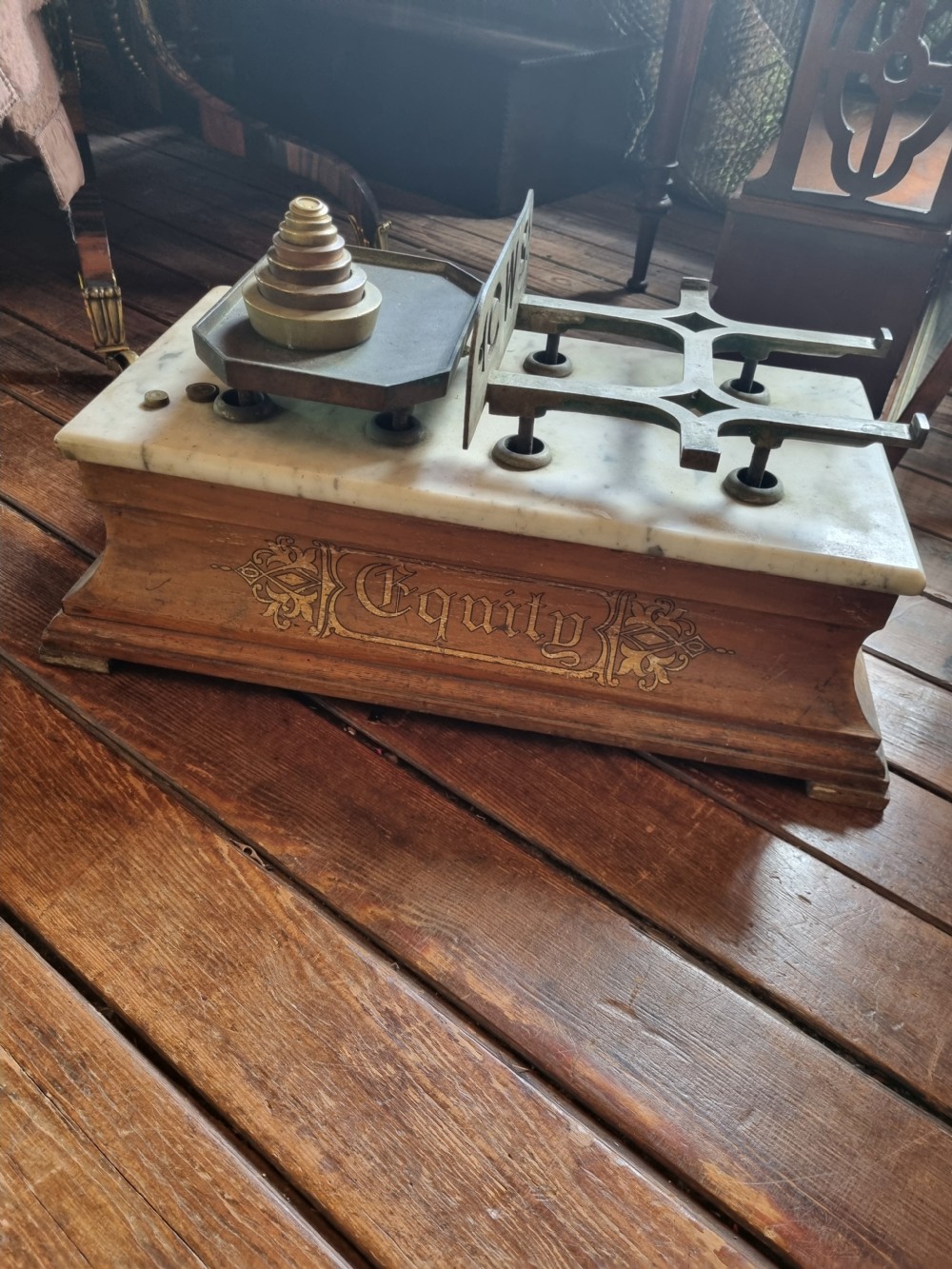 A Victorian grocer balance scale featuring a wooden base with gilded Equity lettering, a white marble slab surface, cast metal framework marked CWS, and nested brass weights. View V
