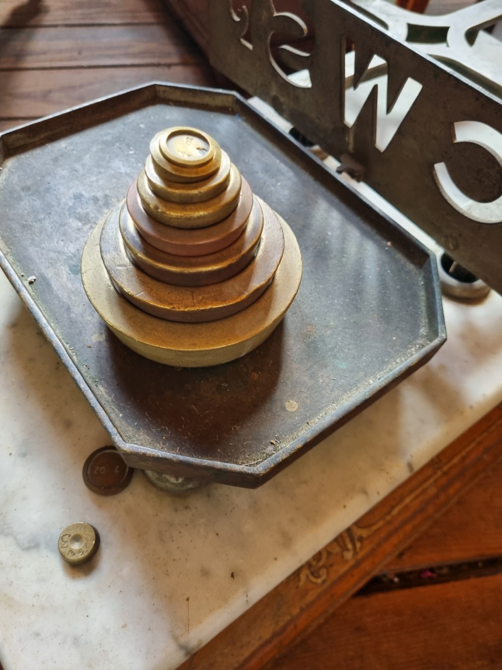 A Victorian grocer balance scale featuring a wooden base with gilded Equity lettering, a white marble slab surface, cast metal framework marked CWS, and nested brass weights. View VI