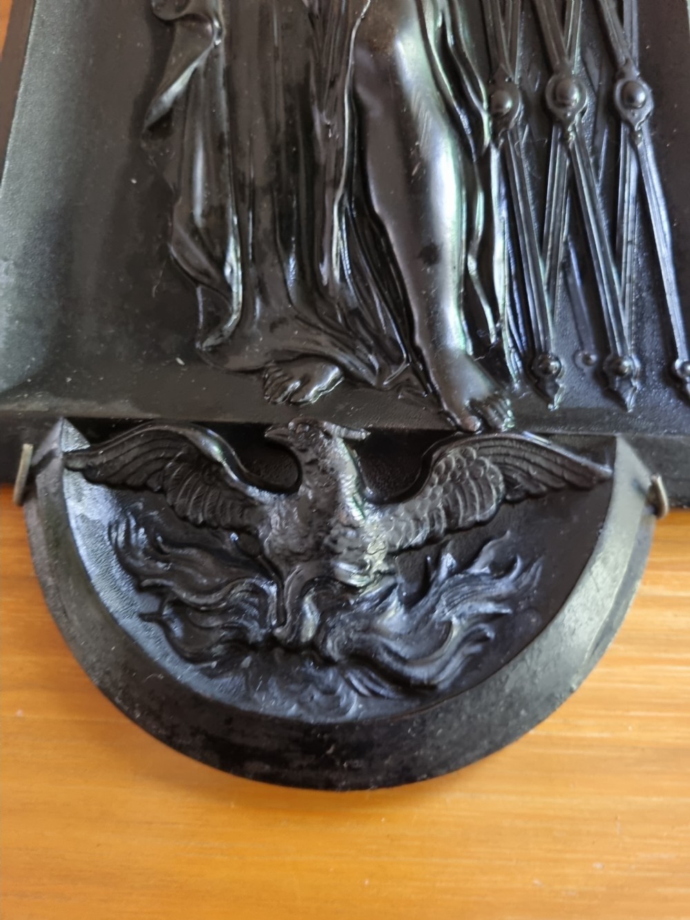 A dark ebonised vertical relief wall plaque depicting the Roman goddess Vesta with classical drapery standing beside a tripod burner with an eagle motif at the base. View V