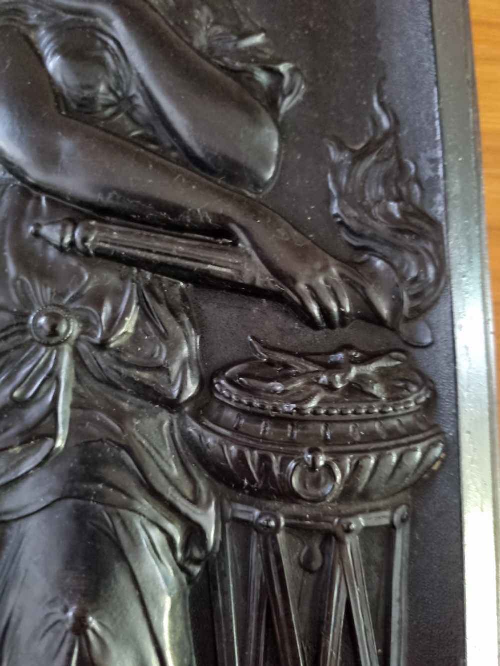 A dark ebonised vertical relief wall plaque depicting the Roman goddess Vesta with classical drapery standing beside a tripod burner with an eagle motif at the base. View VI