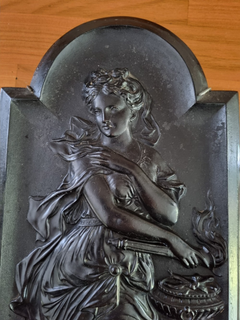 A dark ebonised vertical relief wall plaque depicting the Roman goddess Vesta with classical drapery standing beside a tripod burner with an eagle motif at the base. View VIII