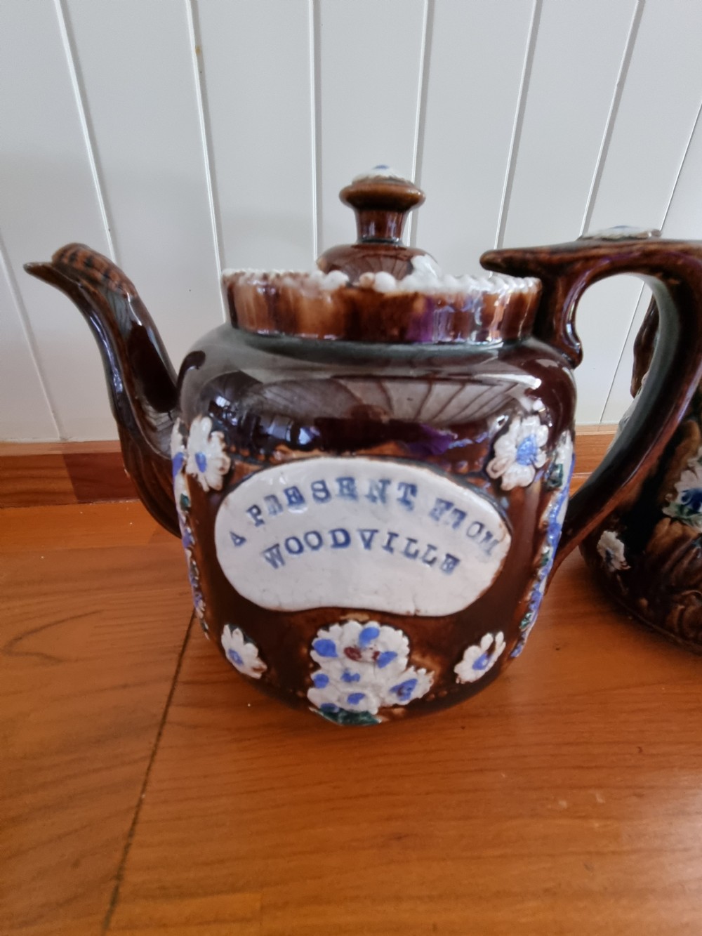A pair of Victorian Measham Bargeware stoneware vessels, including a teapot inscribed A Present From Woodville and a jug inscribed Mrs C Drake 1893, both featuring dark brown treacle glaze and sprigged floral decoration. View II