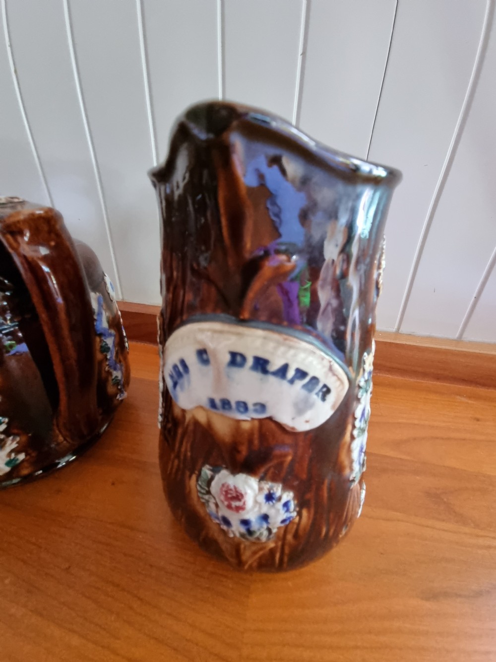 A pair of Victorian Measham Bargeware stoneware vessels, including a teapot inscribed A Present From Woodville and a jug inscribed Mrs C Drake 1893, both featuring dark brown treacle glaze and sprigged floral decoration. View III
