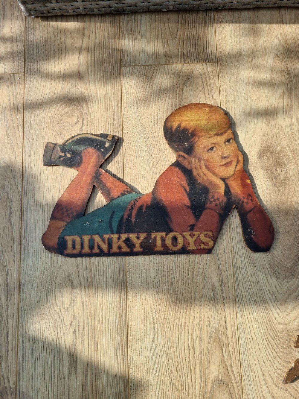 A vintage cardboard counter display sign shaped as a lying boy advertising Dinky Toys. View V