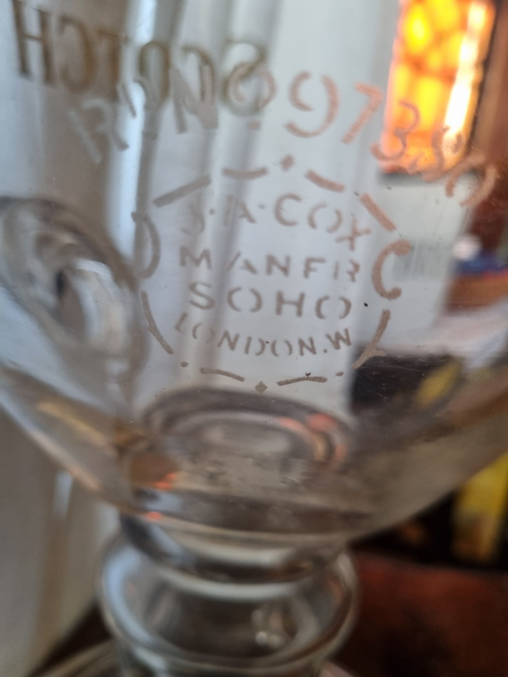 A clear glass Victorian whisky dispenser featuring gilded lettering reading Monopoly Fine Old Scotch Whisky, a brass spigot tap, and a faceted glass spire stopper. View III