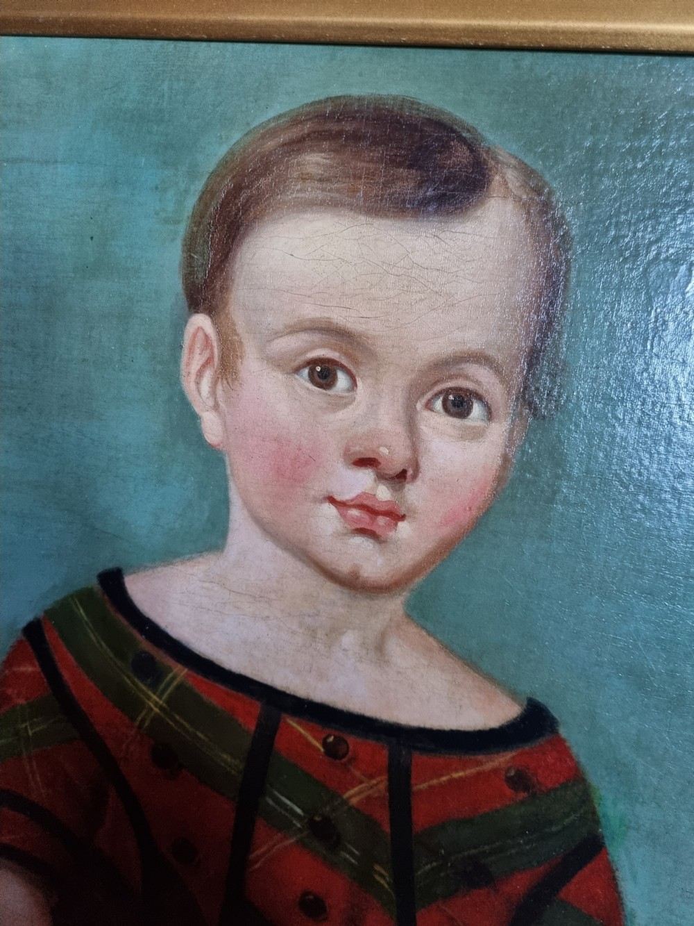 A 19th-century naive oil painting on canvas depicting a standing child in a red and dark blue striped dress with a dog, displayed within a gilded frame. View II