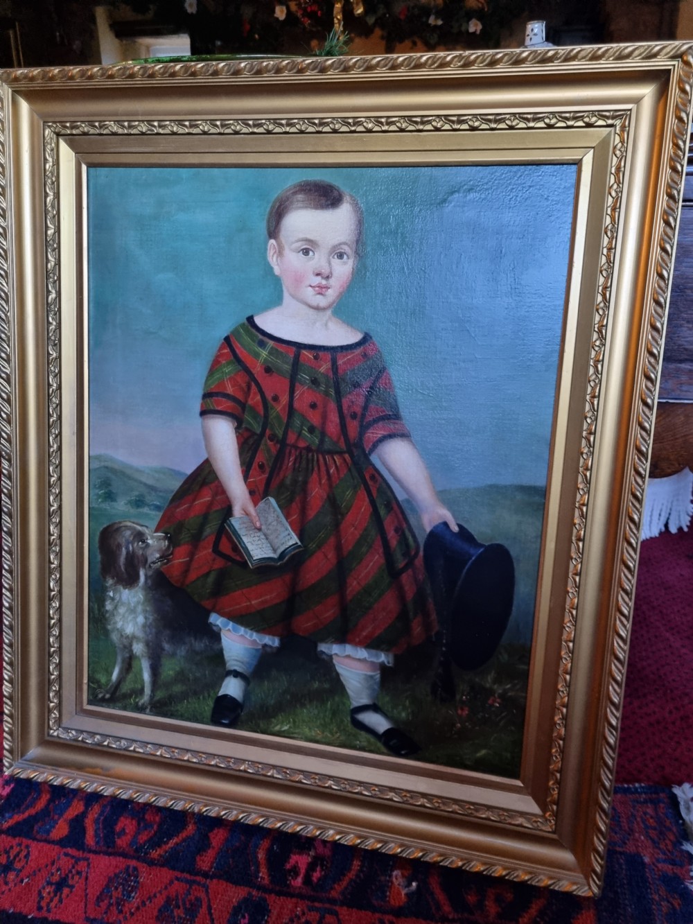 A 19th-century naive oil painting on canvas depicting a standing child in a red and dark blue striped dress with a dog, displayed within a gilded frame. View V