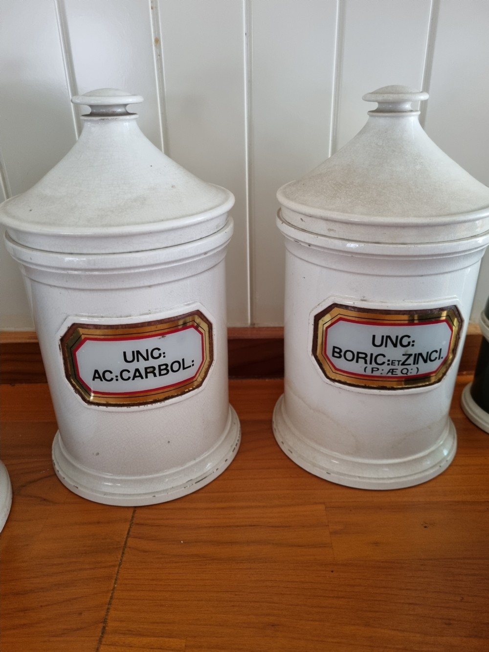 A pair of 19th-century cream glazed ceramic apothecary jars with conical lids and hand-painted gilded Latin labels. View IV