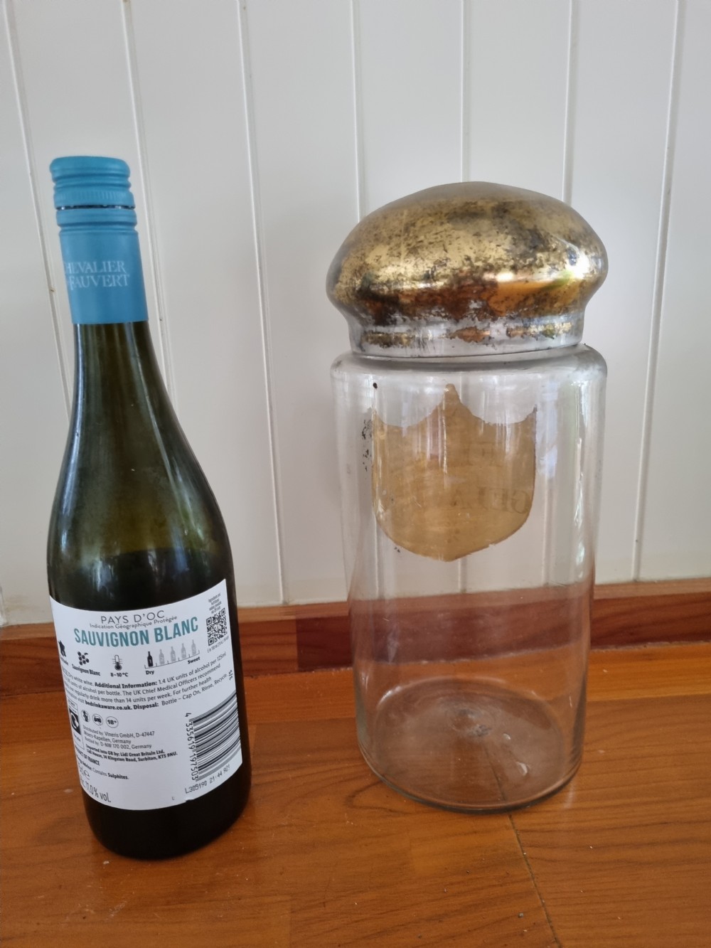 A tall clear glass chemist jar with a domed gold-toned cap and a gold shield label painted with the words Fine Gelatine. View II