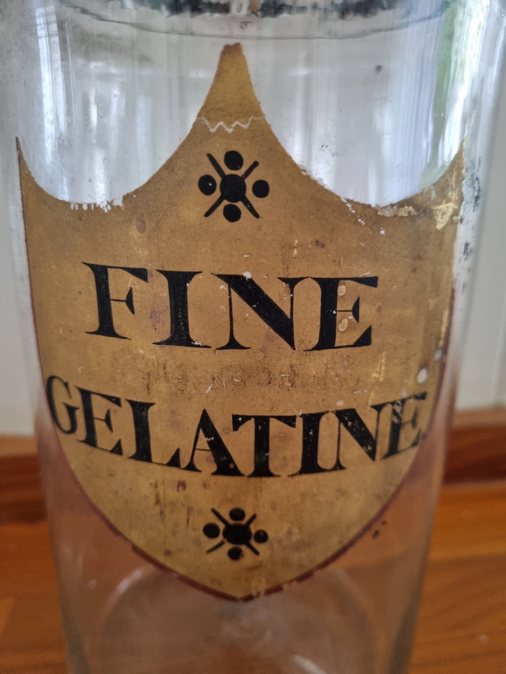A tall clear glass chemist jar with a domed gold-toned cap and a gold shield label painted with the words Fine Gelatine. View III