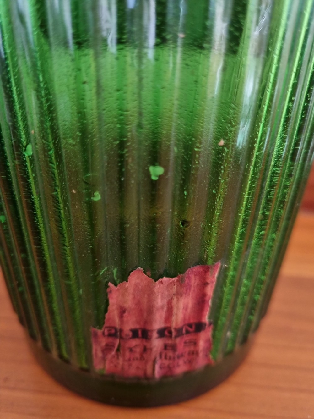 A tall 19th-century emerald green glass chemist jar featuring a ground glass stopper, fluted base, and a red gilded shield label. View III
