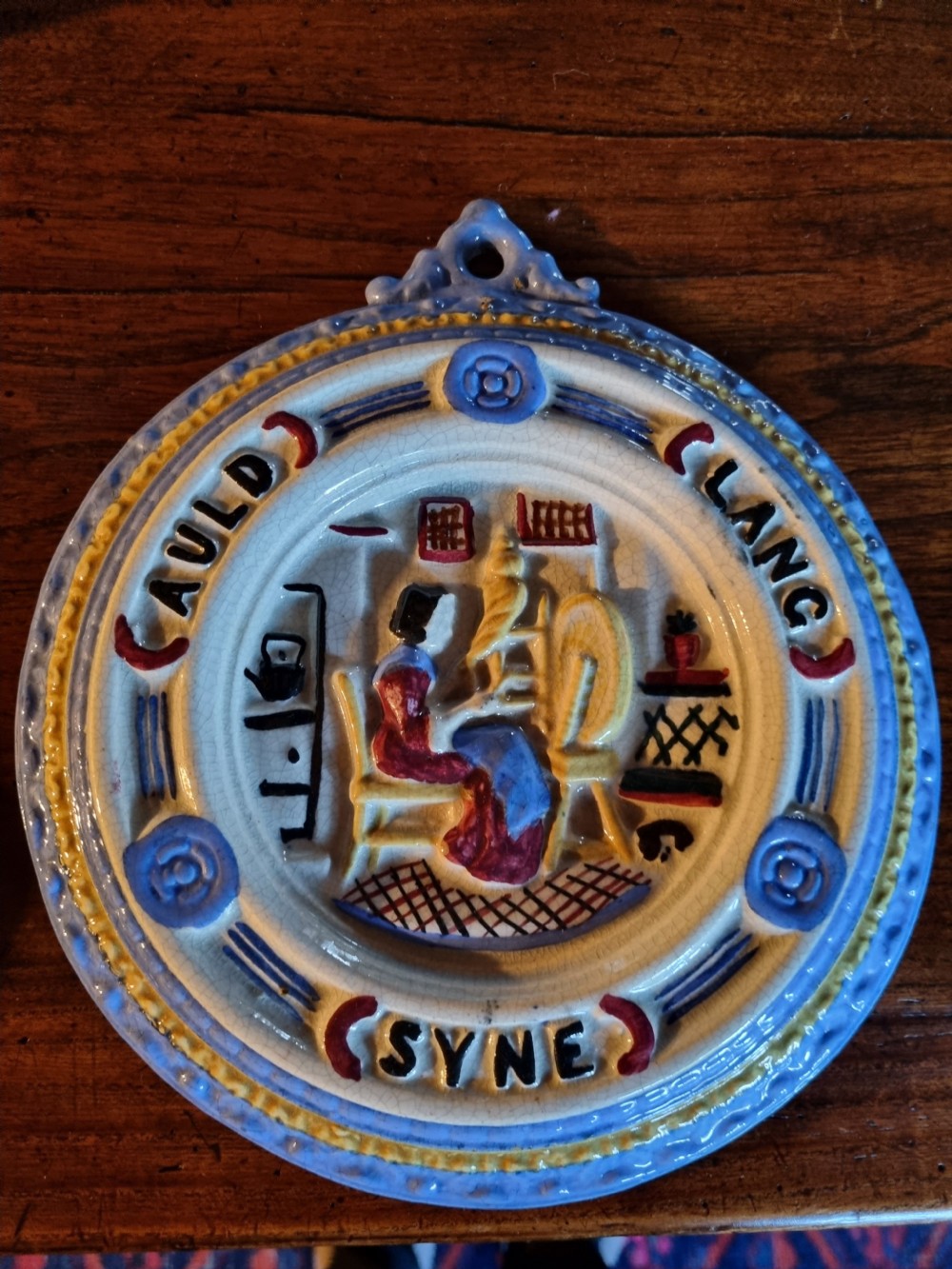 A circular nineteenth-century Scottish ceramic plaque with relief-moulded figures, lettering reading Cauld Lang Syne, and a blue and yellow glazed rim. View V