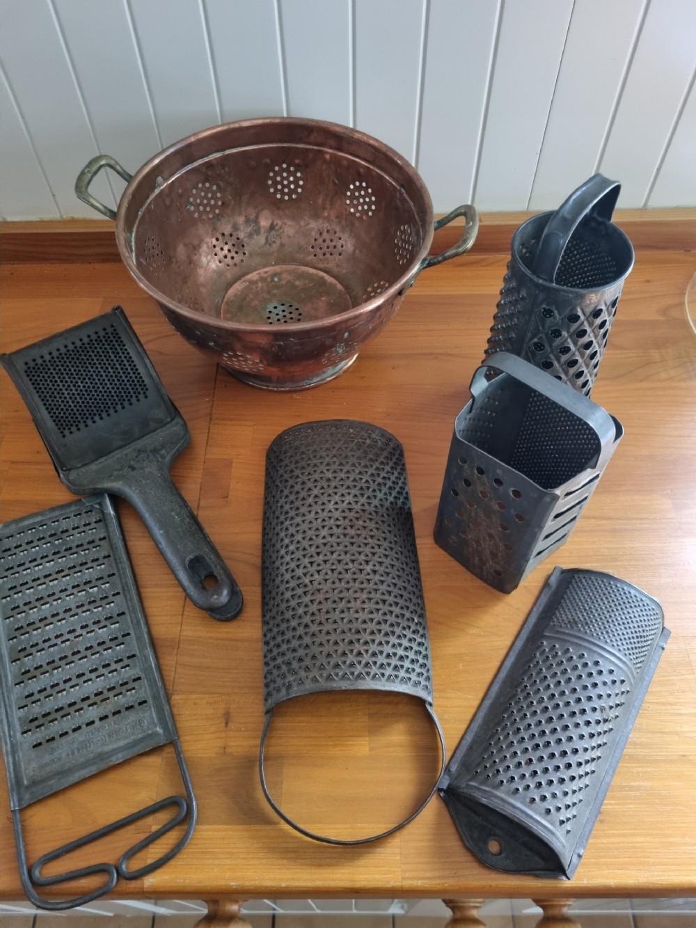 A collection of 19th-century metal kitchenalia featuring a copper colander with brass handles alongside several antique tin graters.